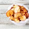 A pile of dried slices of apples in white pouch on wooden background. Dried fruit chips.
