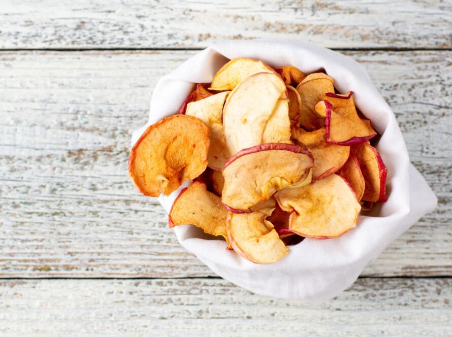 A pile of dried slices of apples in white pouch on wooden background. Dried fruit chips.
